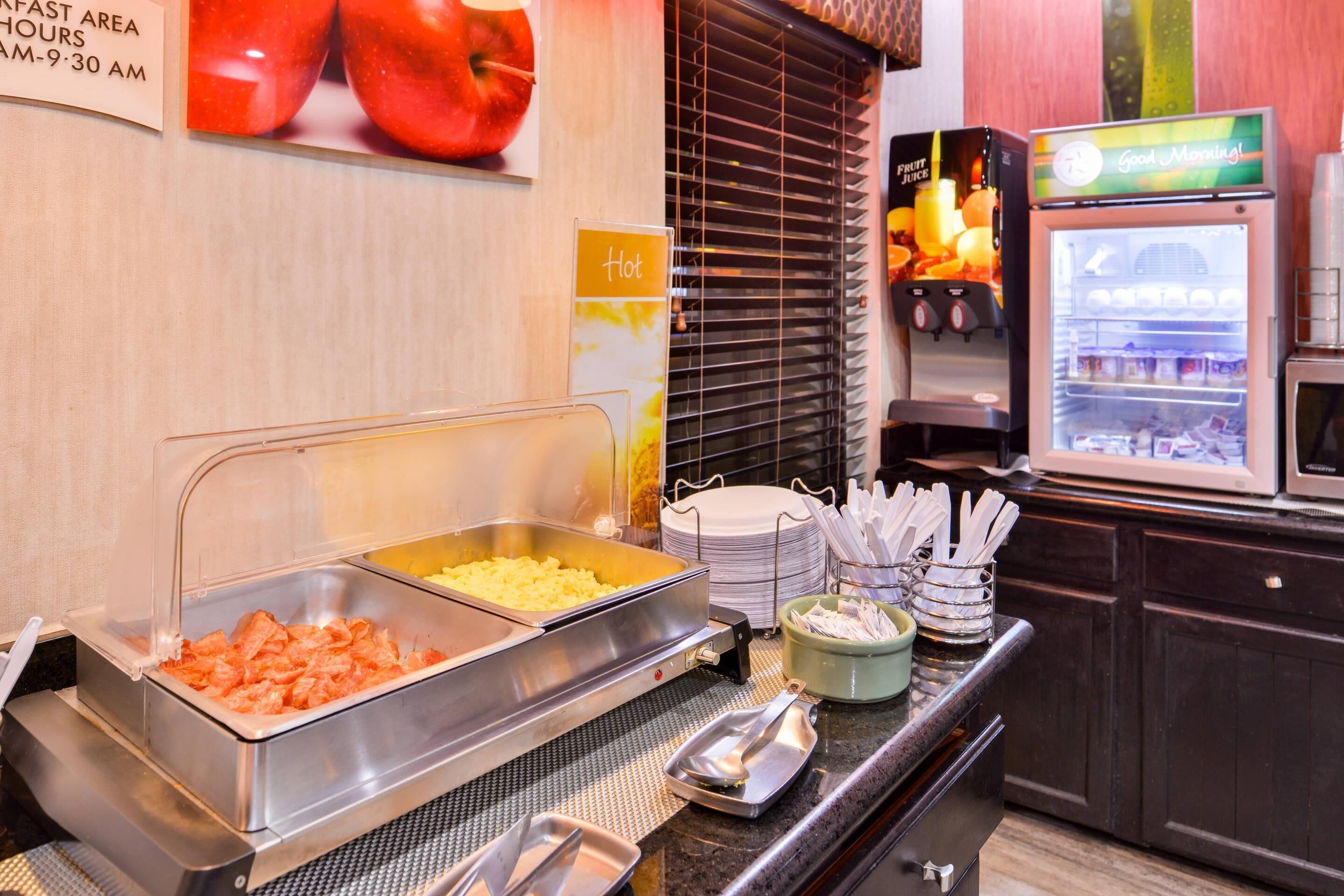 A buffet area with various food options, a refrigerator with beverages, and a sign indicating hot food availability.