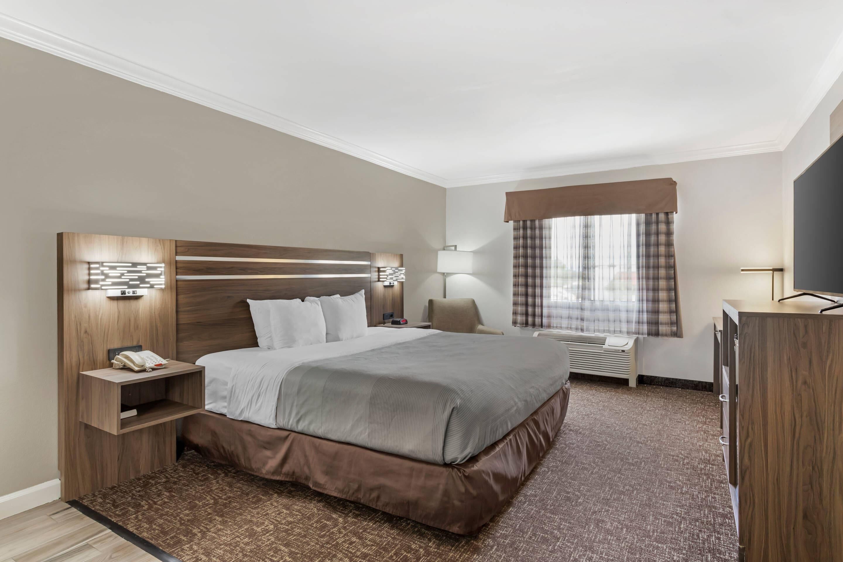A hotel room with a large bed, bedside tables, a desk, a flat-screen TV, and a window with curtains.