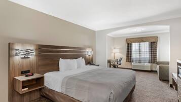 A hotel room with a large bed, a desk, a chair, a nightstand, and a wall-mounted lamp.