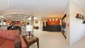 A hotel lobby with a reception desk, a seating area with a sofa and a table, and a dining area in the background. - Quality Inn & Suites Beaumont (Beaumont)