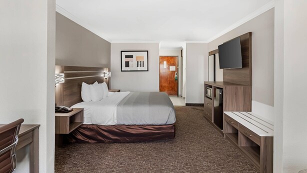 A hotel room with a bed, bedside table, lamp, and a TV. - Quality Inn & Suites Beaumont (Beaumont)