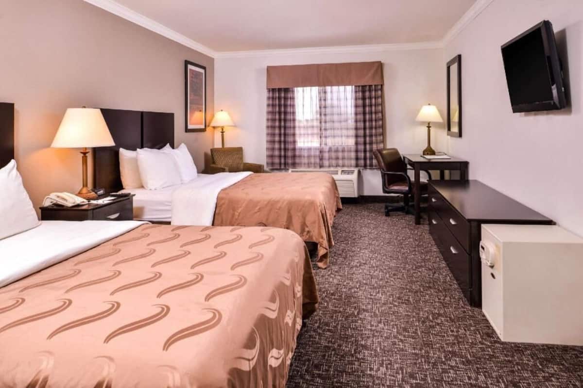 A hotel room with two beds, a desk, a chair, a television, and a window with curtains.