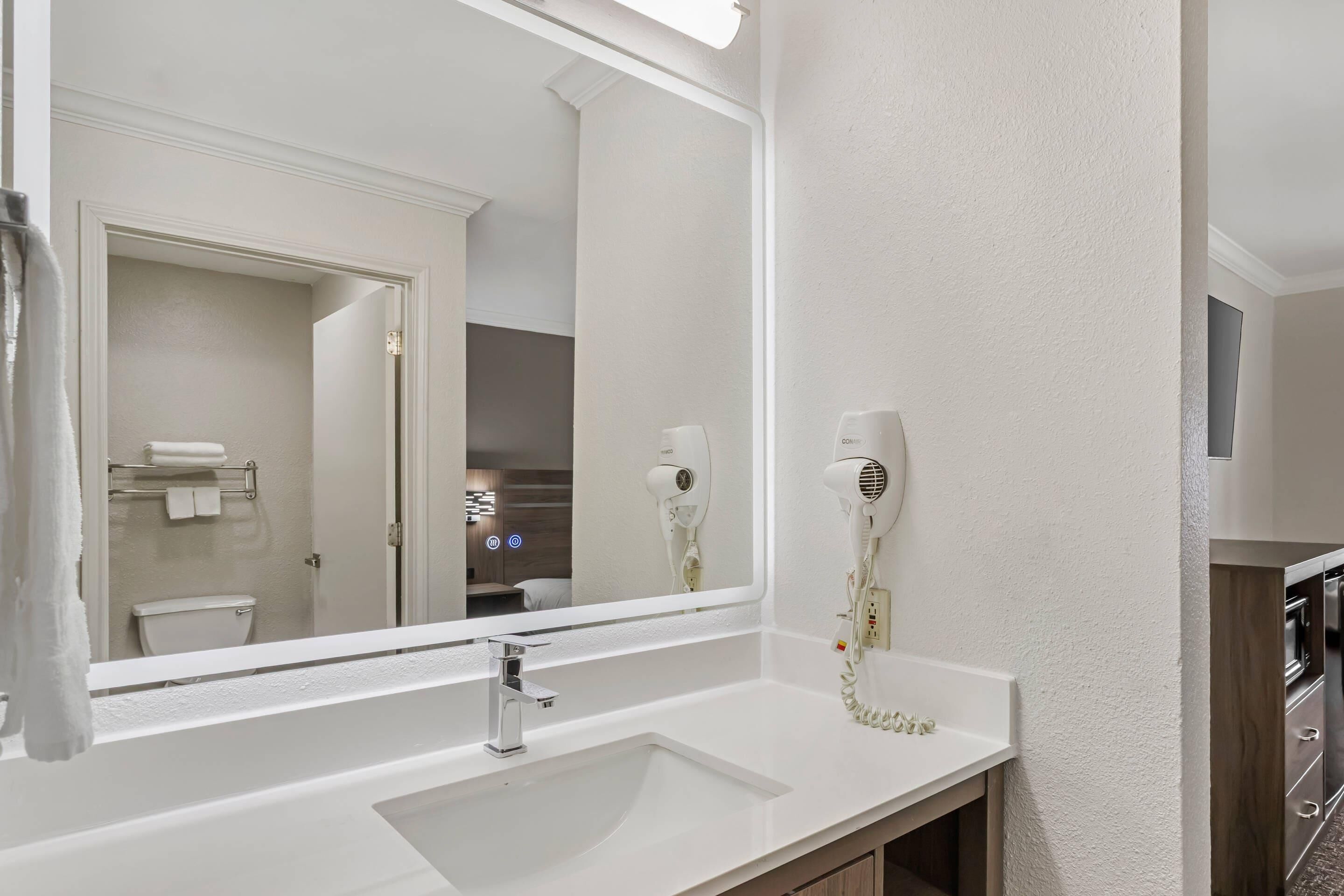 A bathroom with a white sink, a mirror, and a hairdryer mounted on the wall.