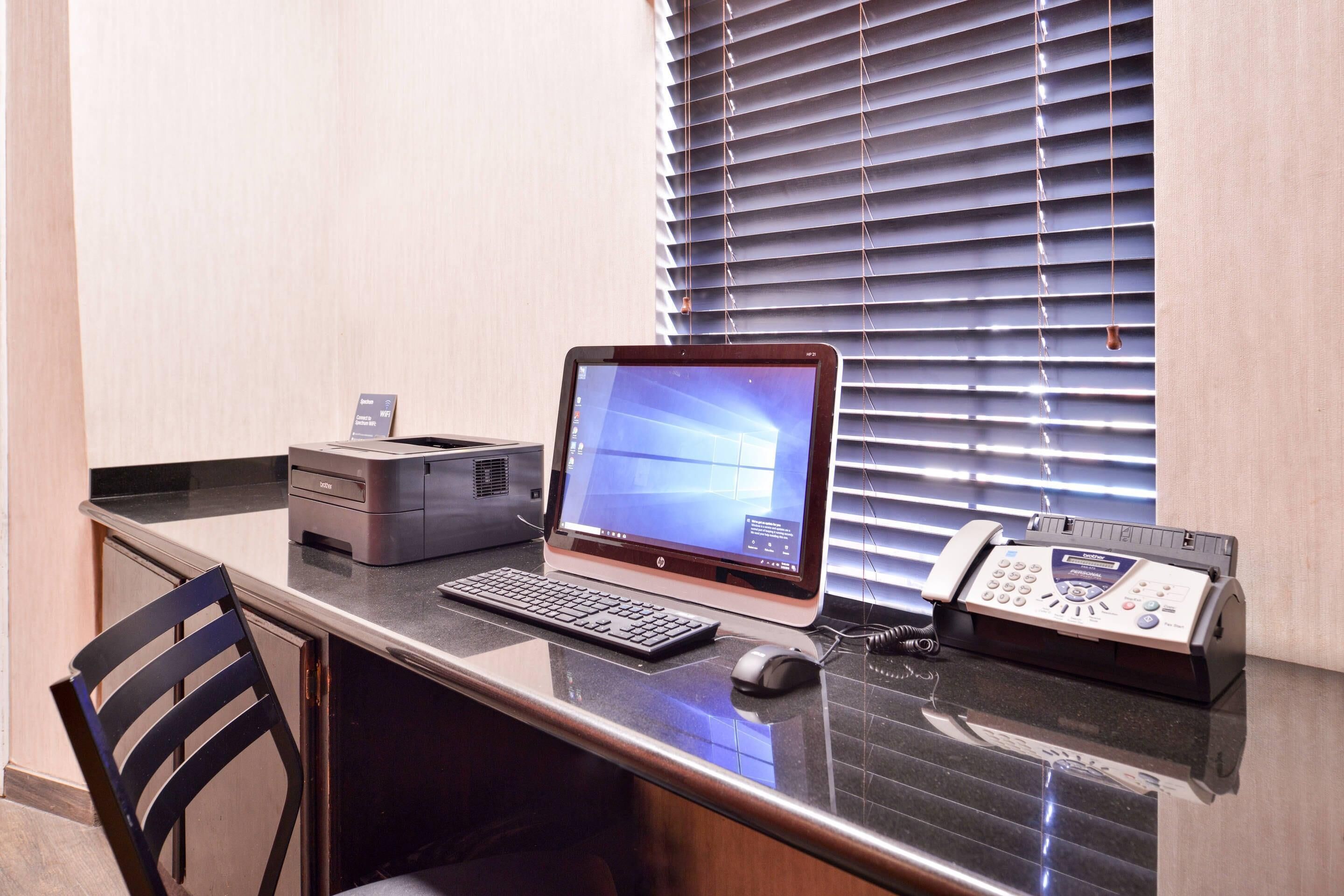 Ein Hotelrezeptionstresen mit einem Computer, einem Drucker, einem Telefon und einem Stuhl.