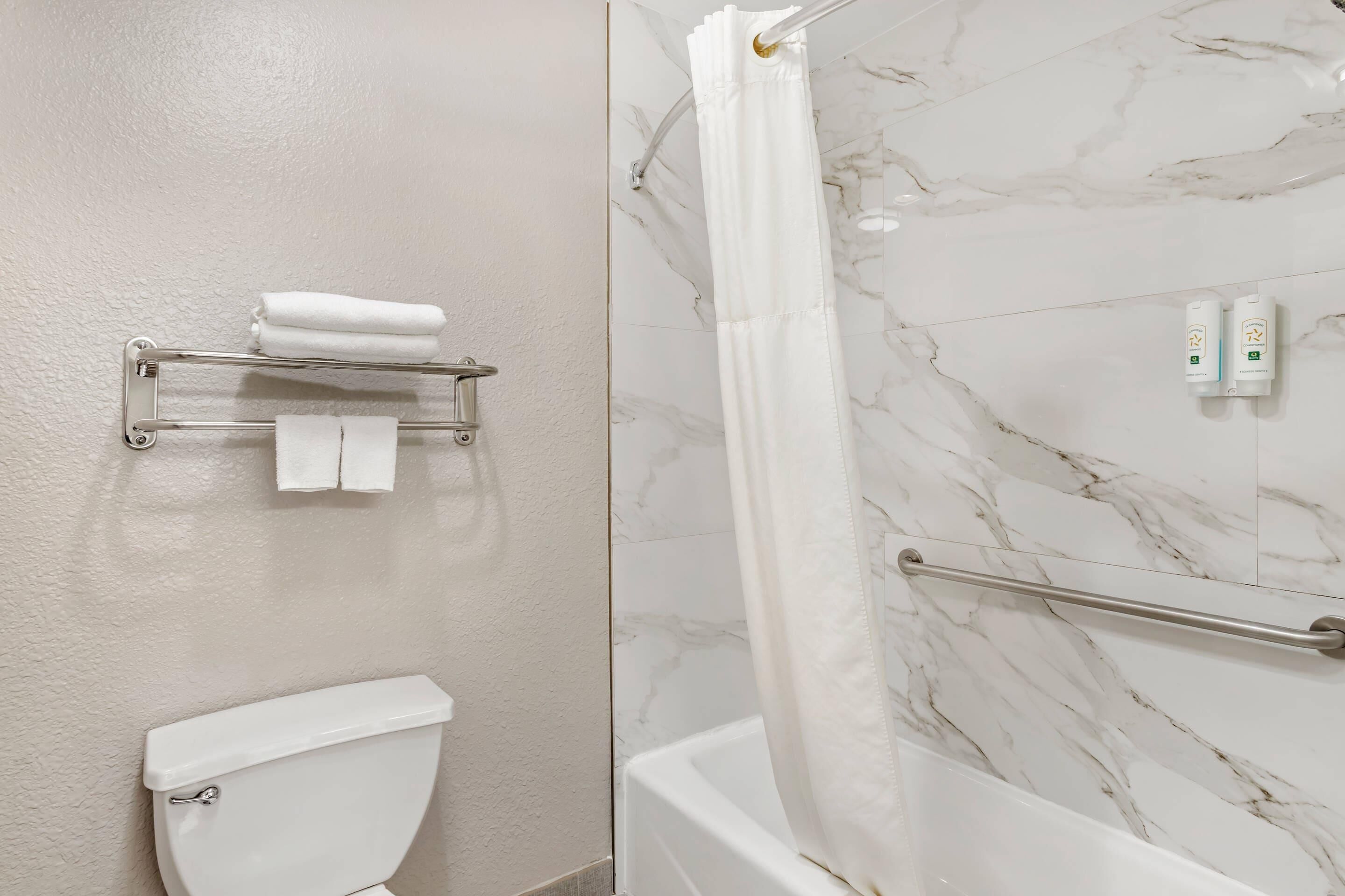 A bathroom with a toilet, towel rack, shower curtain, and a marble wall.