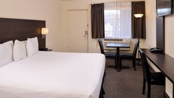 A hotel room with a large bed, a desk, a chair, a television, and a window with curtains.
