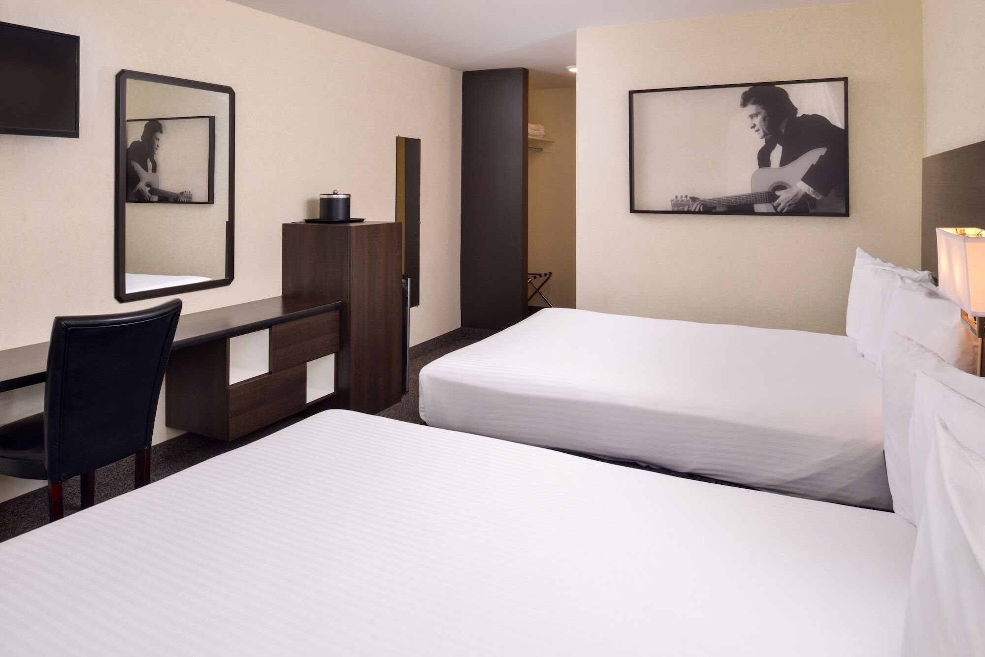 A hotel room with two beds, a desk, a chair, a wardrobe, and a mirror.