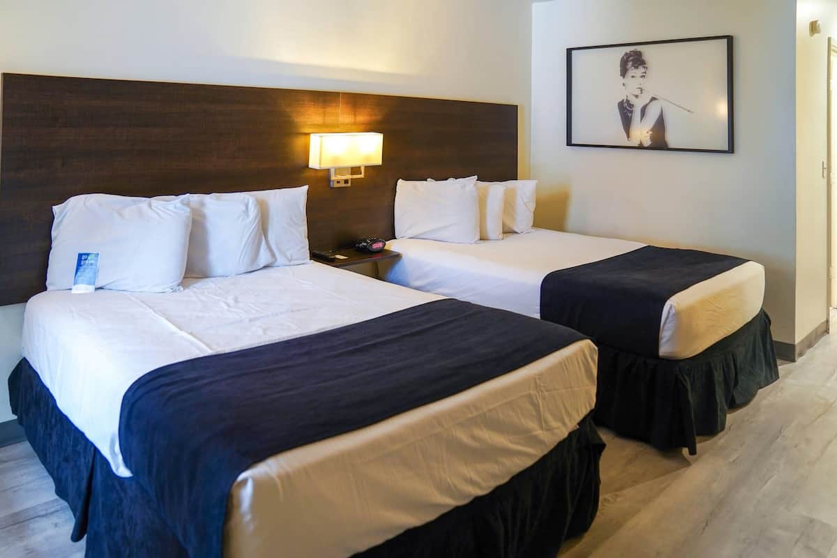A hotel room with two beds, a nightstand, a lamp, and a framed picture on the wall.