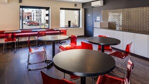 Un intérieur moderne avec des sièges rouges, des tables rondes et de grandes fenêtres donnant sur la rue.