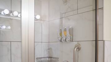 A bathroom with white marble tiles, a shower with a handheld showerhead, and a glass-enclosed mirror.
