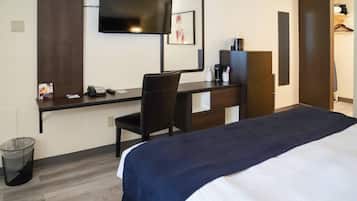 A hotel room with a bed, desk, chair, TV, and a trash can.