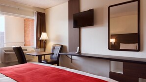 Une chambre d’hôtel avec un lit, un bureau, une chaise, une télévision et un miroir.