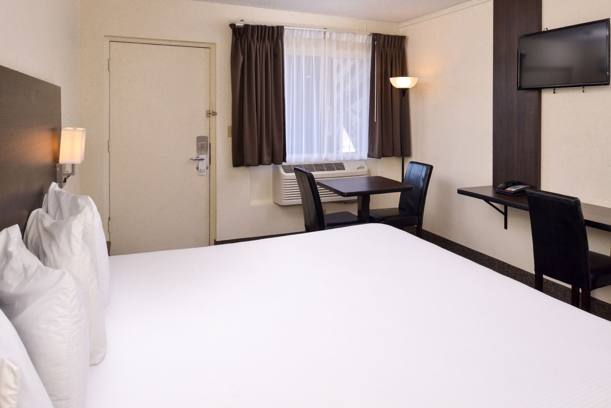 A hotel room with a bed, a desk, a chair, a television, and an air conditioning unit.