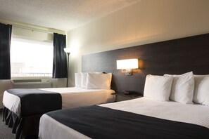 A hotel room with two beds, a bedside table with a lamp, and a window with curtains.