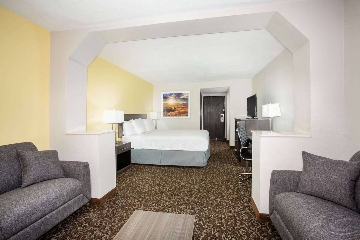 Ein Hotelzimmer mit einem Bett, zwei Sesseln, einem Schreibtisch und einem Gemälde an der Wand.