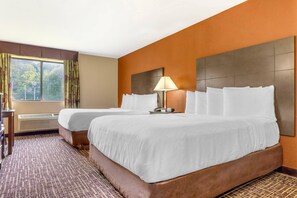 A hotel room with two beds, a desk, a lamp, and a window with curtains.