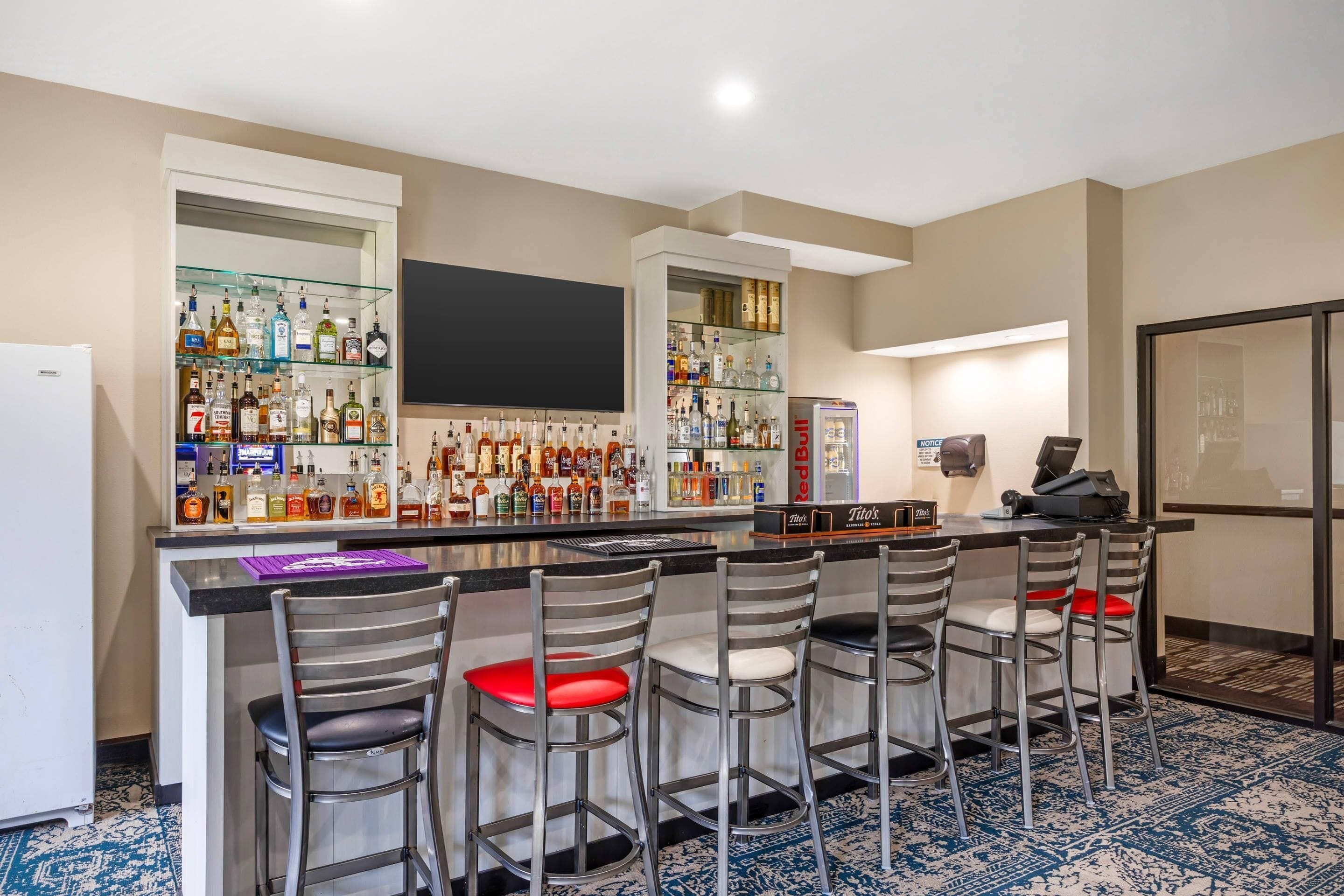 A bar area with multiple stools, a flat-screen TV, and a variety of liquor bottles.