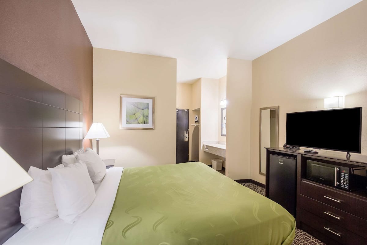 Una habitación de hotel con una cama, televisión, escritorio y espejo.