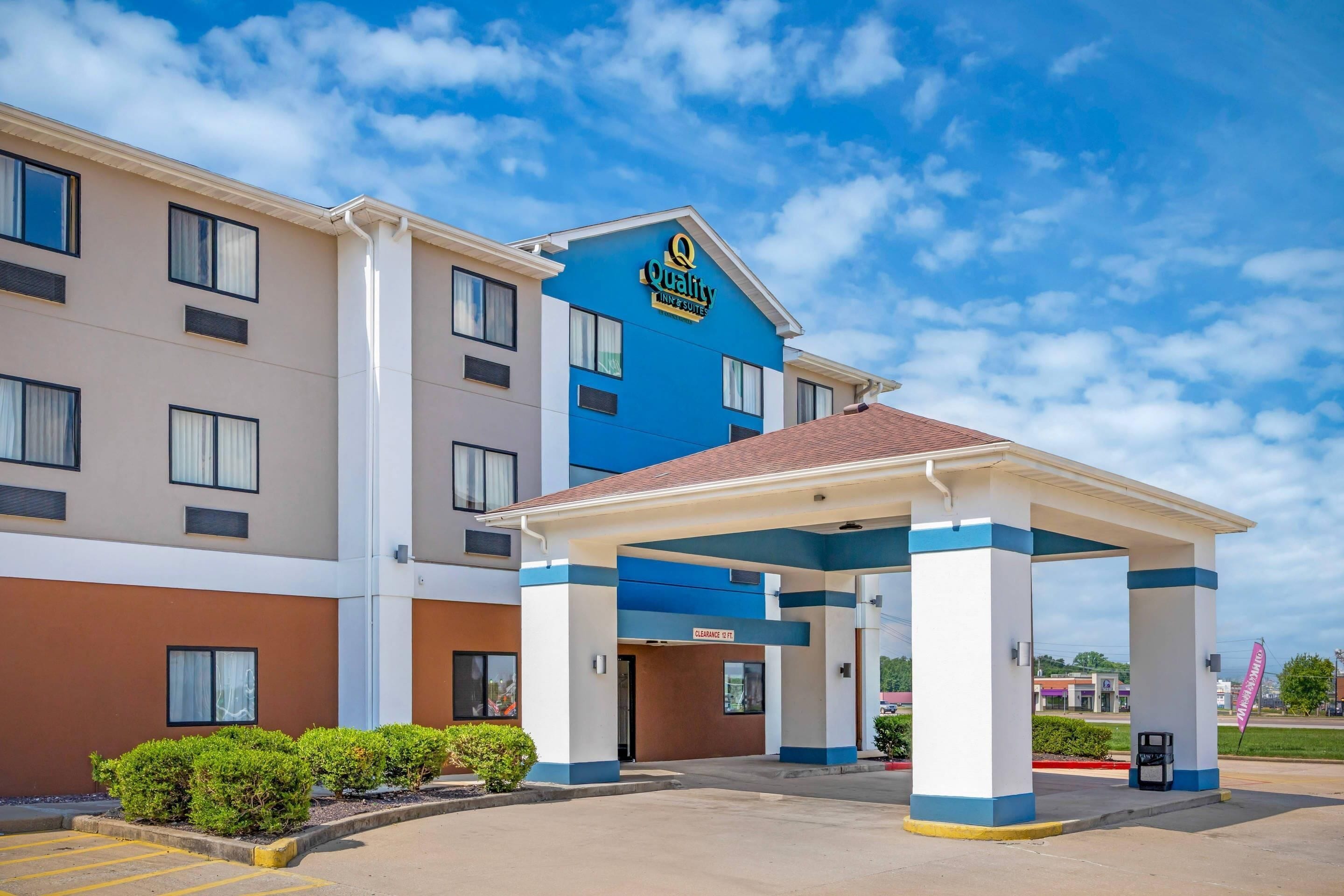 Un hotel con fachada azul y blanca, un acceso cubierto y un cielo despejado.