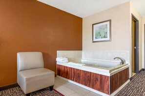 A bathroom with a bathtub, a chair, and a framed picture on the wall.