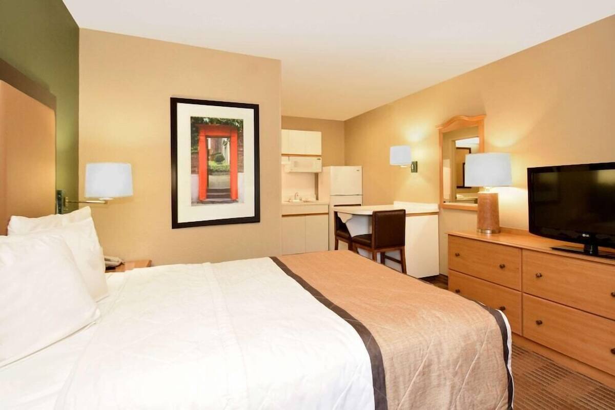 A hotel room with a bed, desk, TV, and a framed picture on the wall.