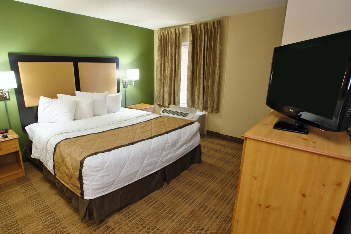 A hotel room with a large bed, a desk with a computer, a television, and a window with curtains.