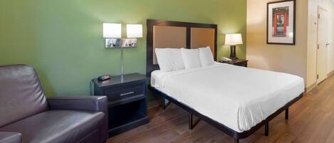 A hotel room with a bed, a nightstand, a lamp, a chair, and a framed picture on the wall.
