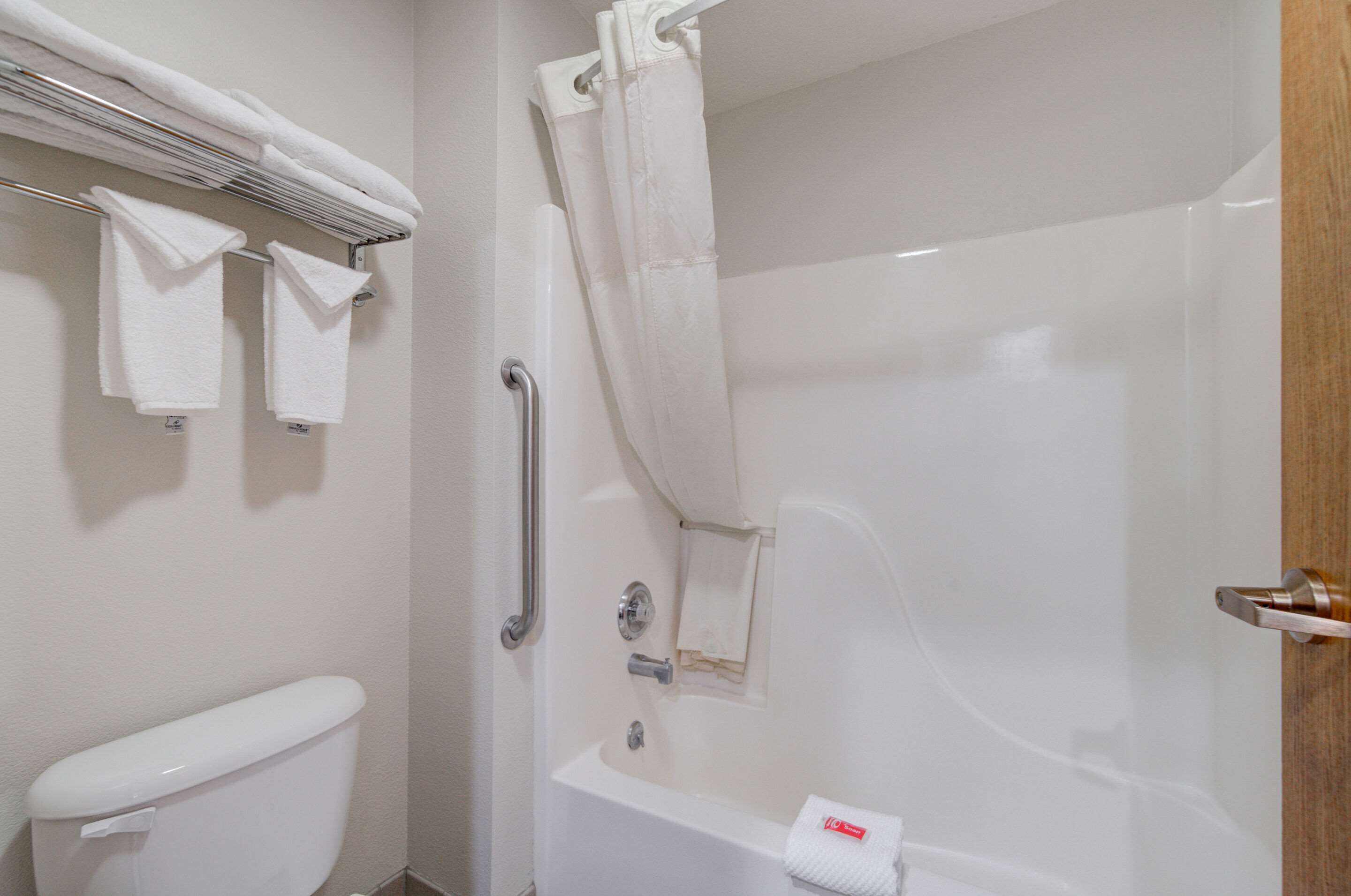 A bathroom with a toilet, a shower with a curtain, and a towel rack with towels.