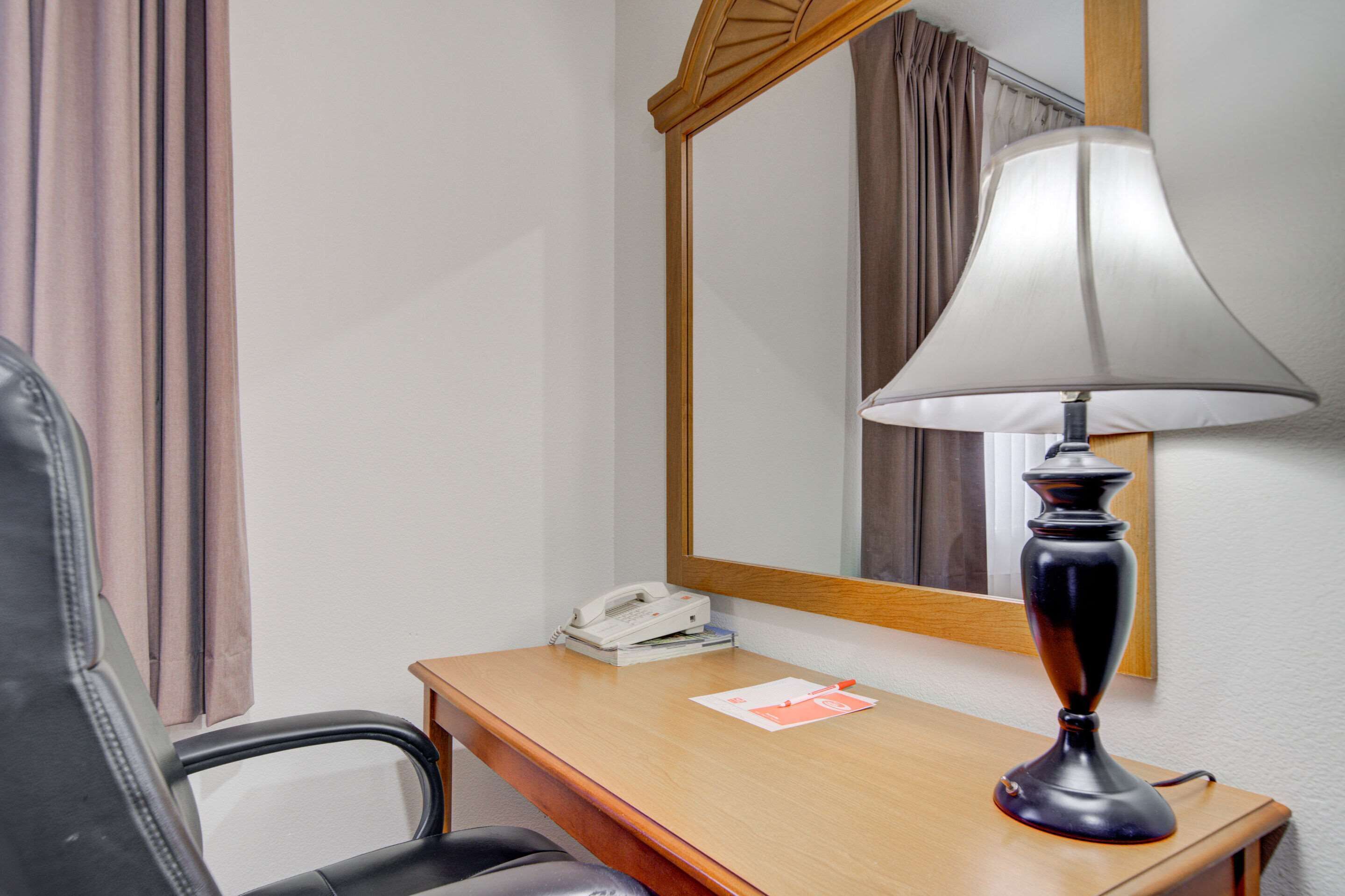 Une chambre d’hôtel avec un bureau en bois, un téléphone, une lampe et un miroir.