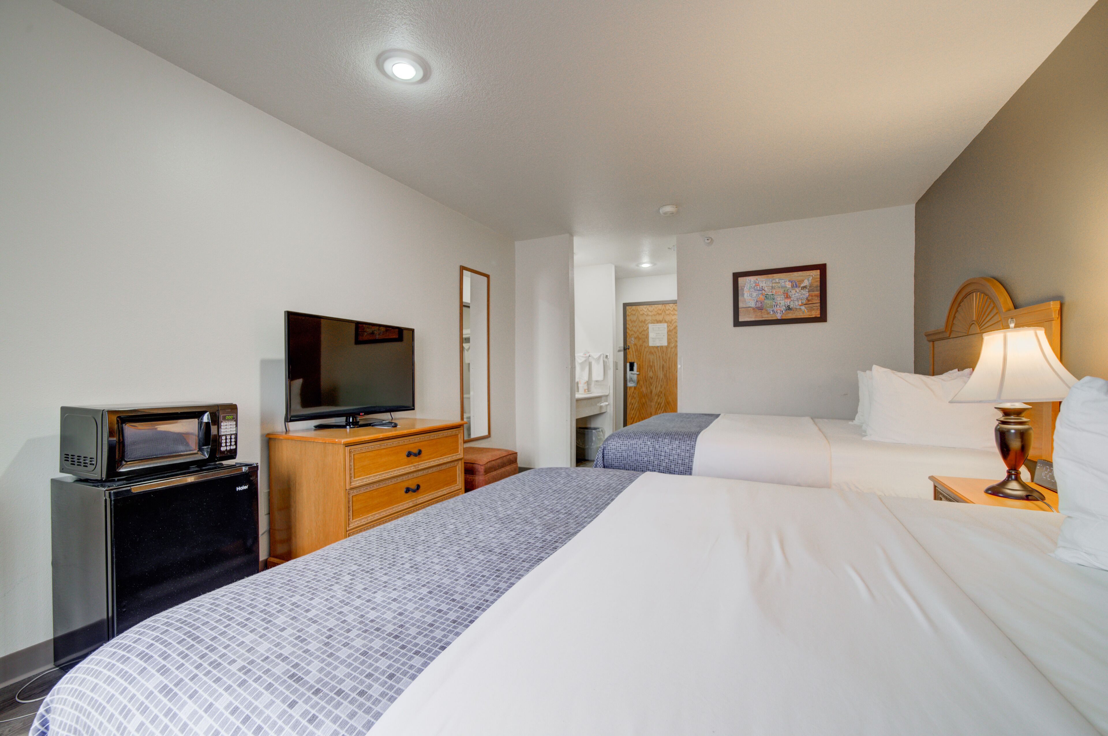 A hotel room with two beds, a TV, a microwave, a wooden dresser, and a lamp.