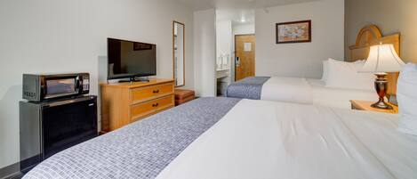 A hotel room with two beds, a TV, a microwave, a wooden dresser, and a lamp.