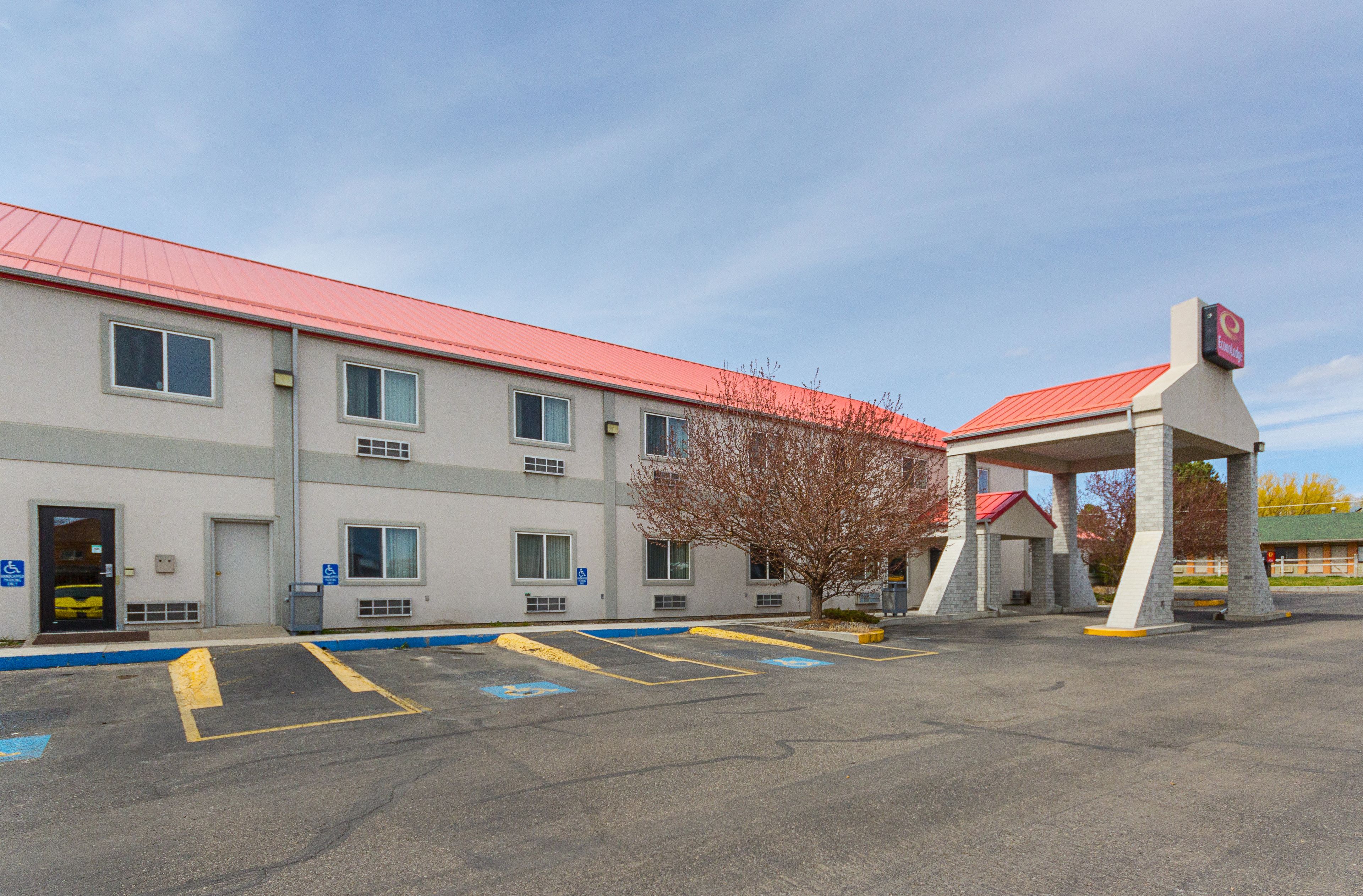 Un motel avec un toit rouge, une station-service et un parking avec des places délimitées.