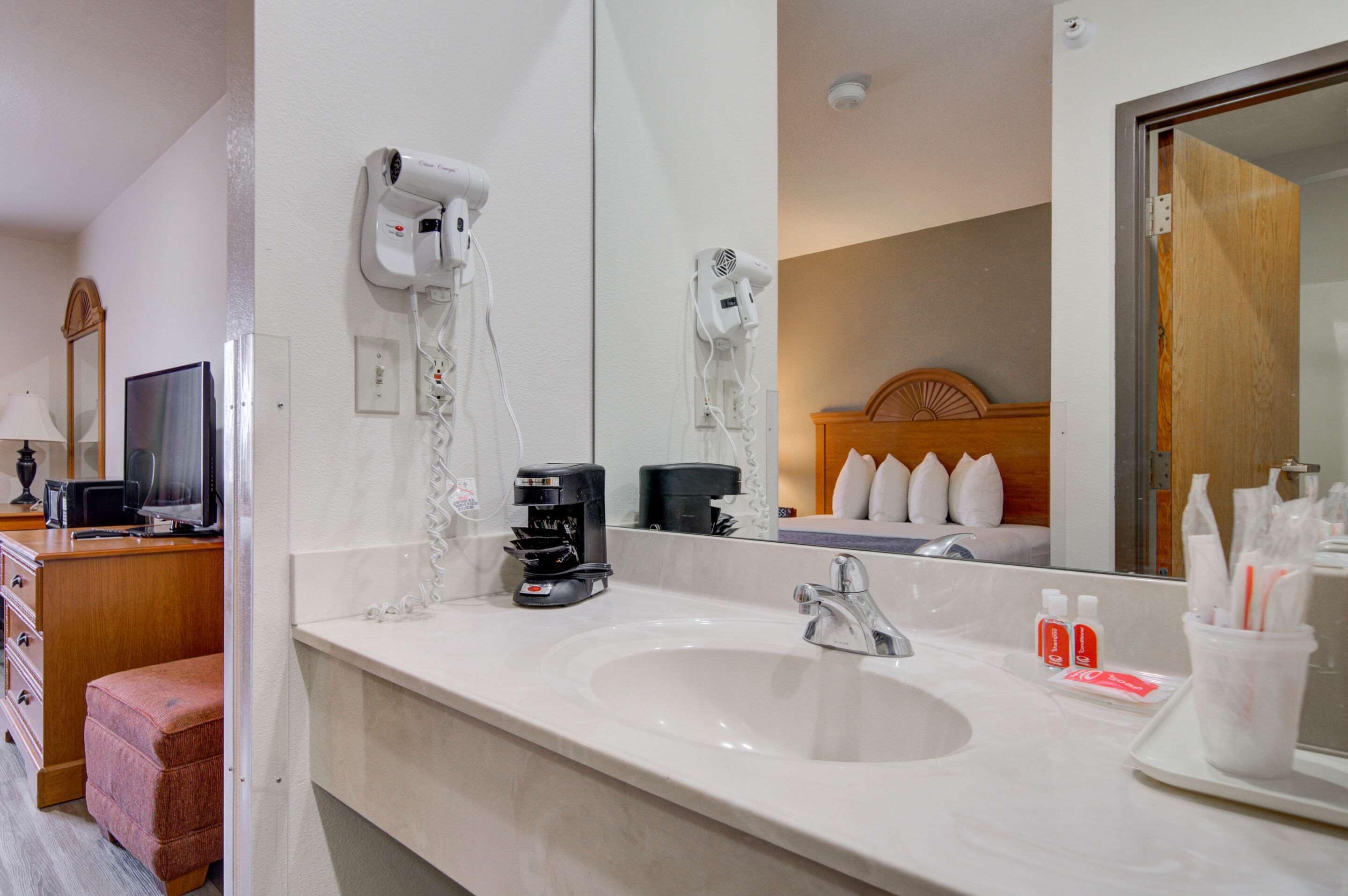 Casa de banho de hotel com um espelho grande, lavatório, secador de cabelo, máquina de café e produtos de higiene pessoal.