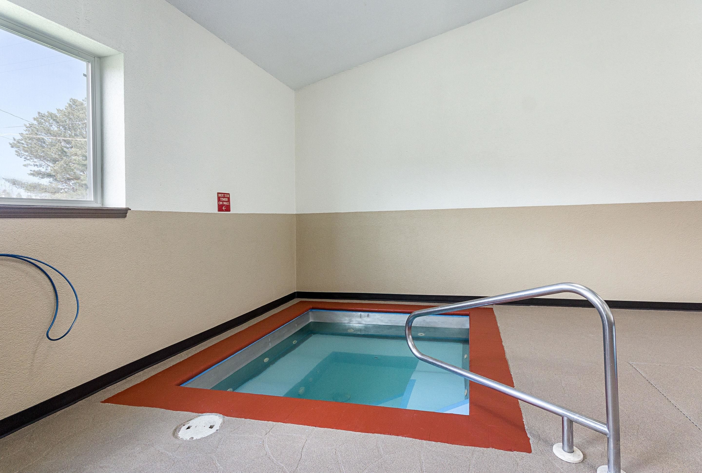 A small indoor pool with a metal ladder, a window, and a red safety sign on the wall.