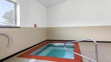 A small indoor pool with a metal ladder, a window, and a red safety sign on the wall.