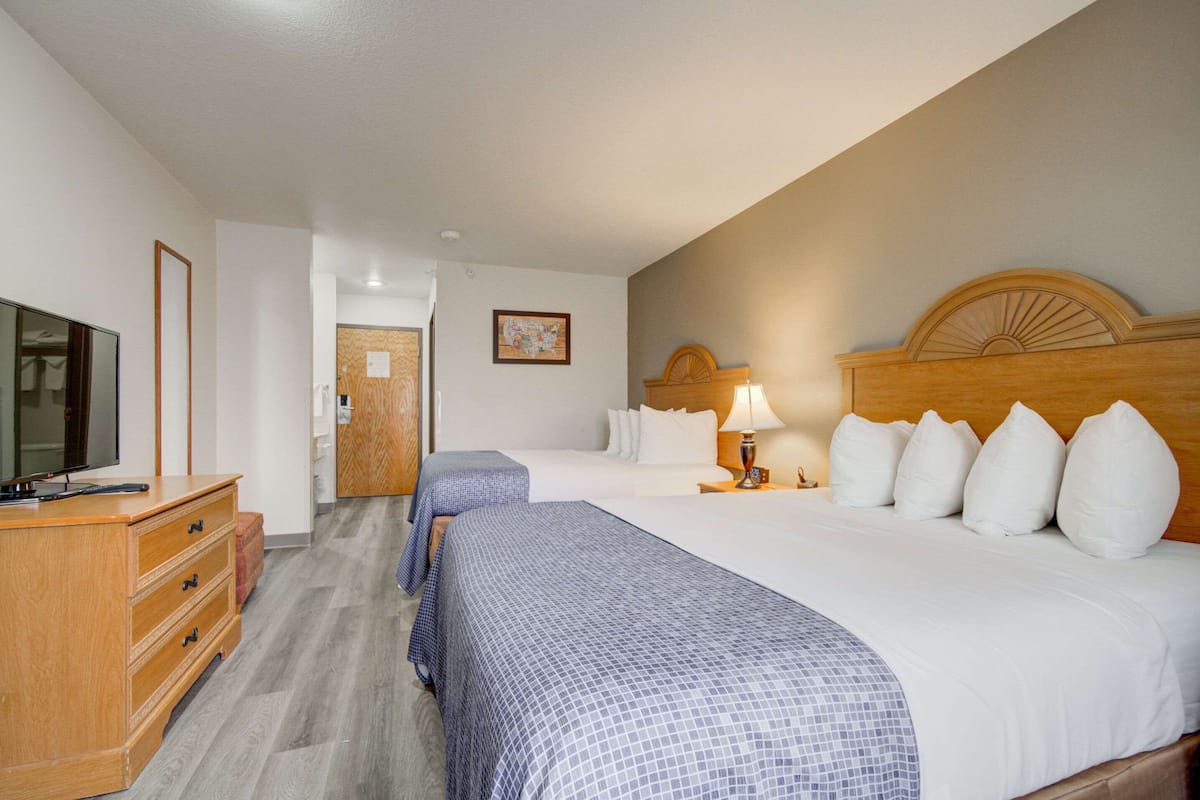 Une chambre d’hôtel avec deux lits, une commode en bois, un téléviseur et un tableau encadré au mur.