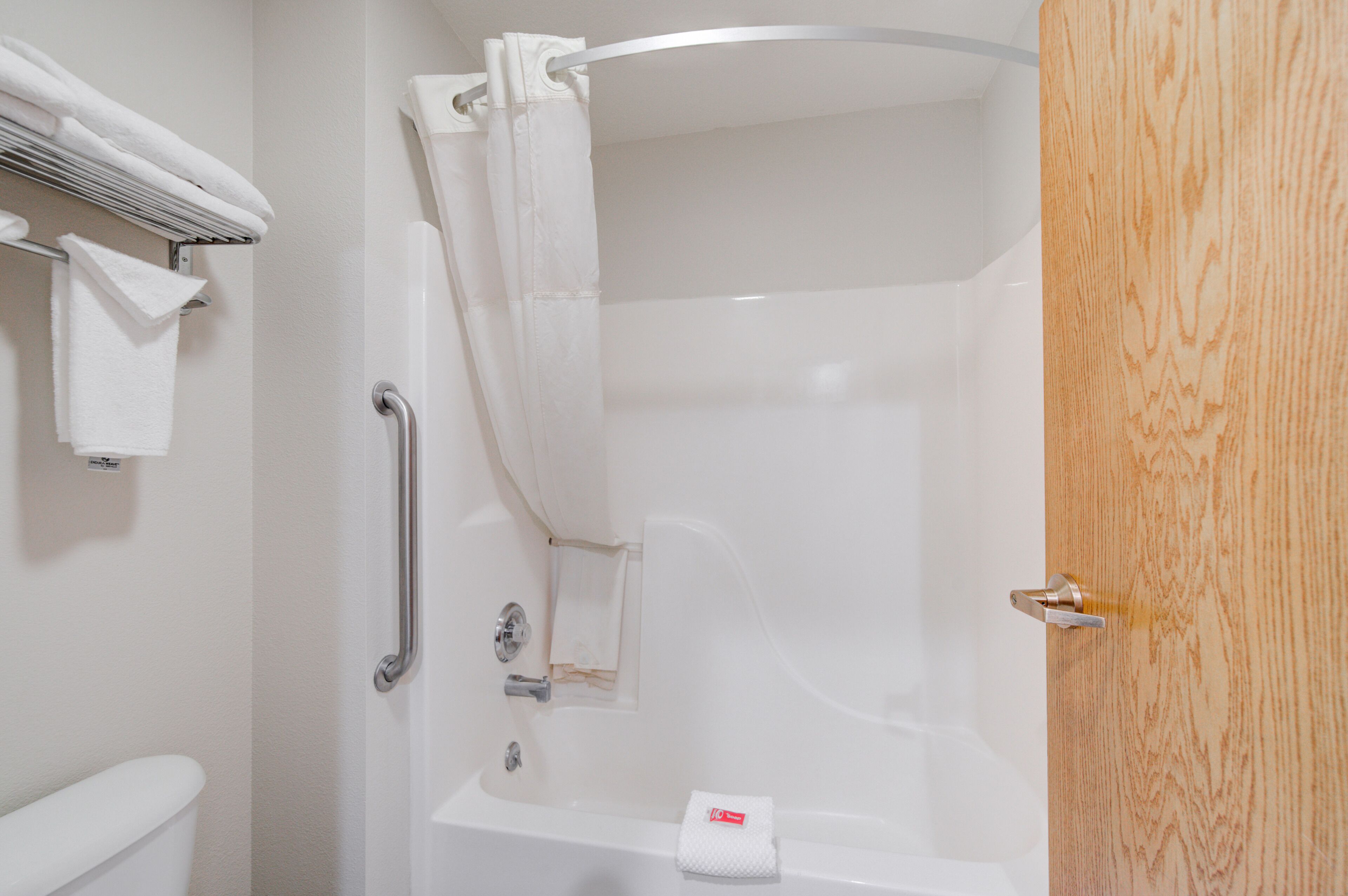 Un baño con bañera, cortina de ducha, toallero y puerta de madera.