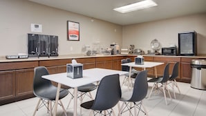 A kitchenette with a microwave, toaster, and coffee maker. There are four tables with chairs, and a trash can is visible. - Econo Lodge Livingston Gateway to Yellowstone (Livingston)