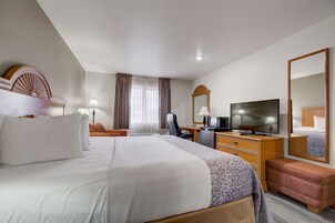 A hotel room with a large bed, a desk with a television, a dresser, and a mirror.
