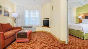 A hotel room with a sofa, a small table, a television, a bed, and a patterned carpet. - Sonesta Simply Suites Houston Brookhollow (Houston)