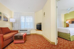 Een hotelkamer met een bank, een tafeltje, een televisie, een bed en een kamerbreed tapijt met dessin.