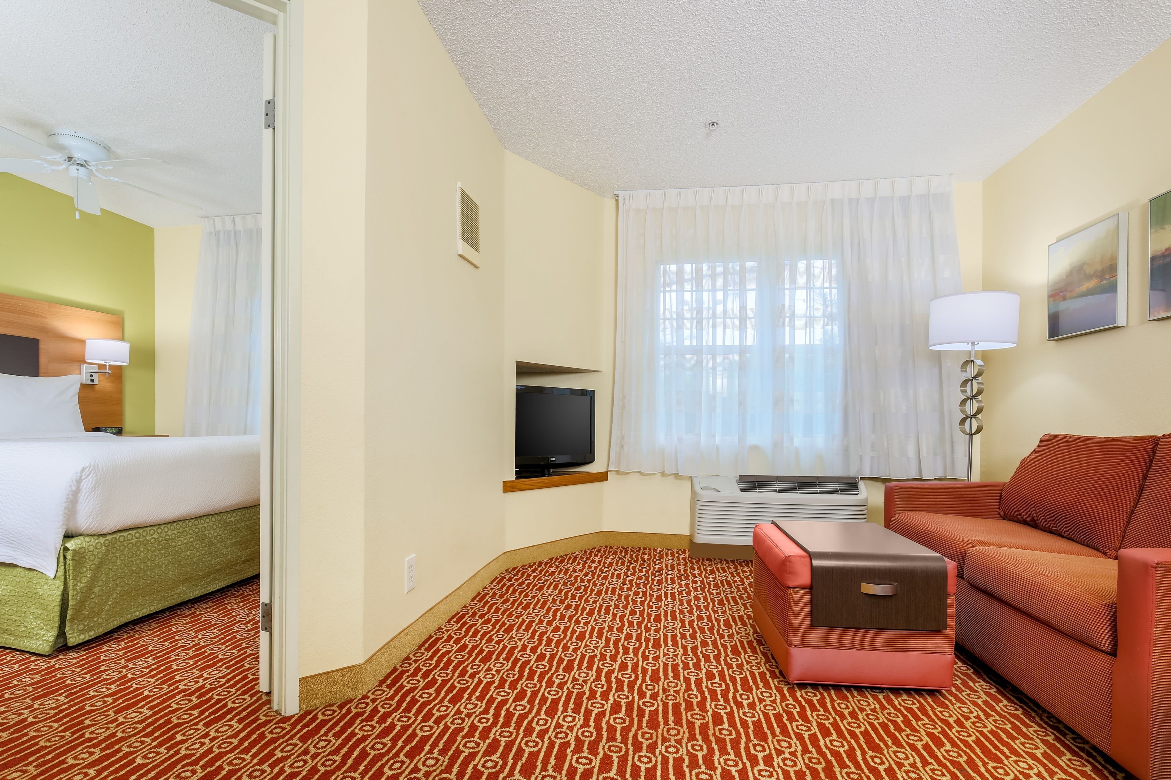 A hotel room with a bed, a sofa, a TV, and a window with curtains.