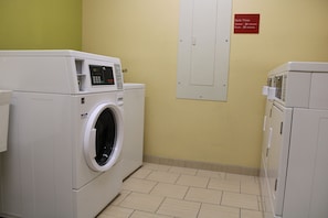 Een wasserette met een voorlader wasmachine en droger, een bedieningspaneel op de wasmachine en een bord met wasprogramma tijden aan de muur.