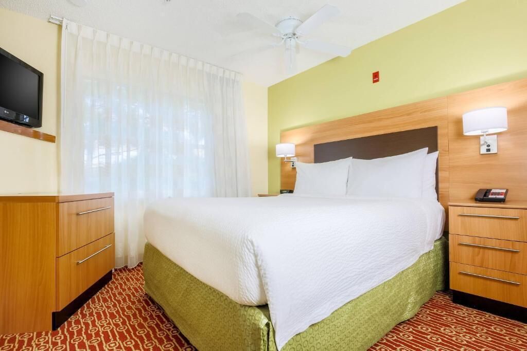 Una habitación de hotel con cama, televisor, escritorio y ventilador de techo.