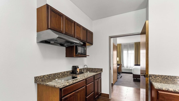 Cocina compacta con armarios de madera, campana extractora de acero inoxidable, microondas y encimera de granito.