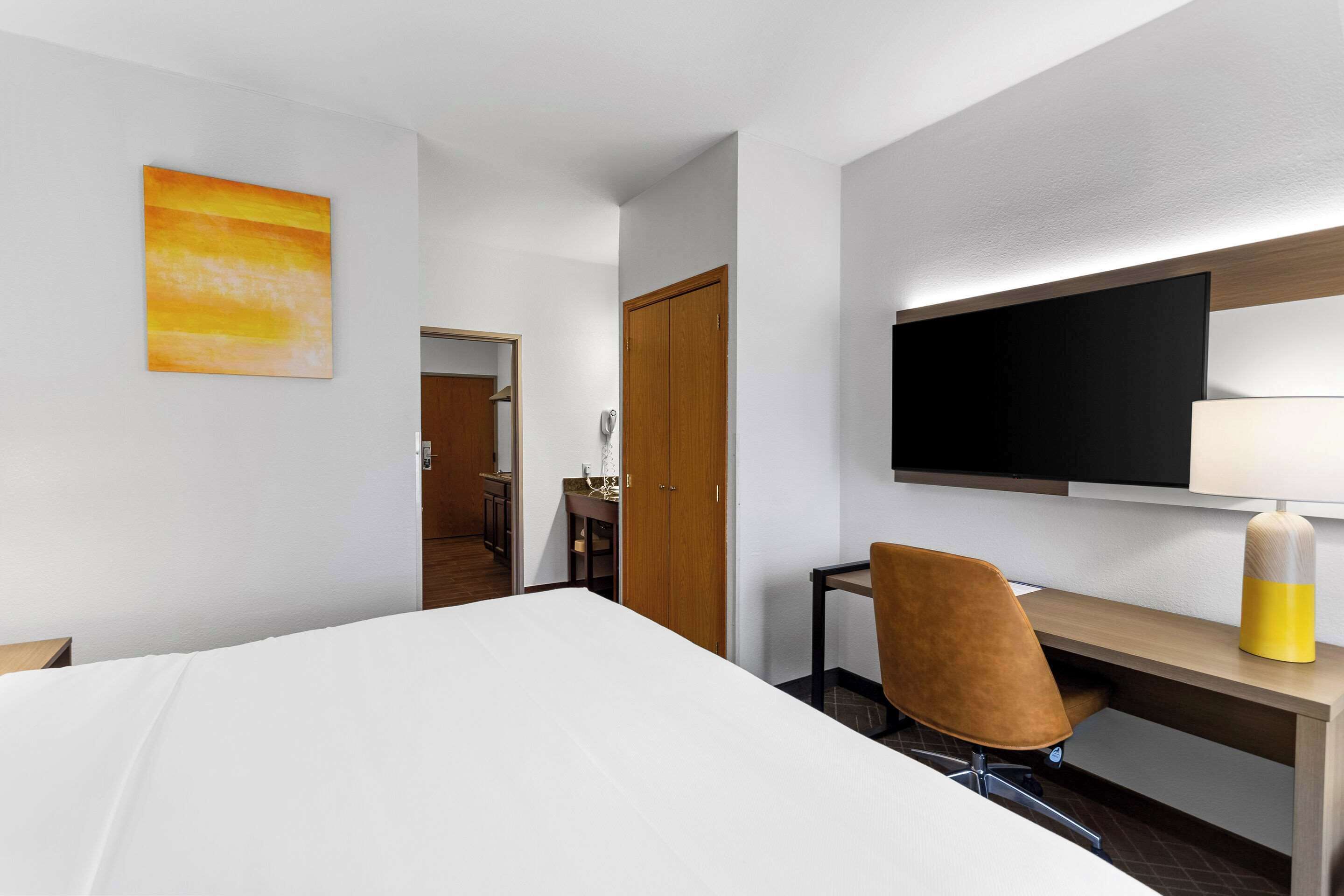 A hotel room with a bed, a desk with a chair, a television, and a painting on the wall.