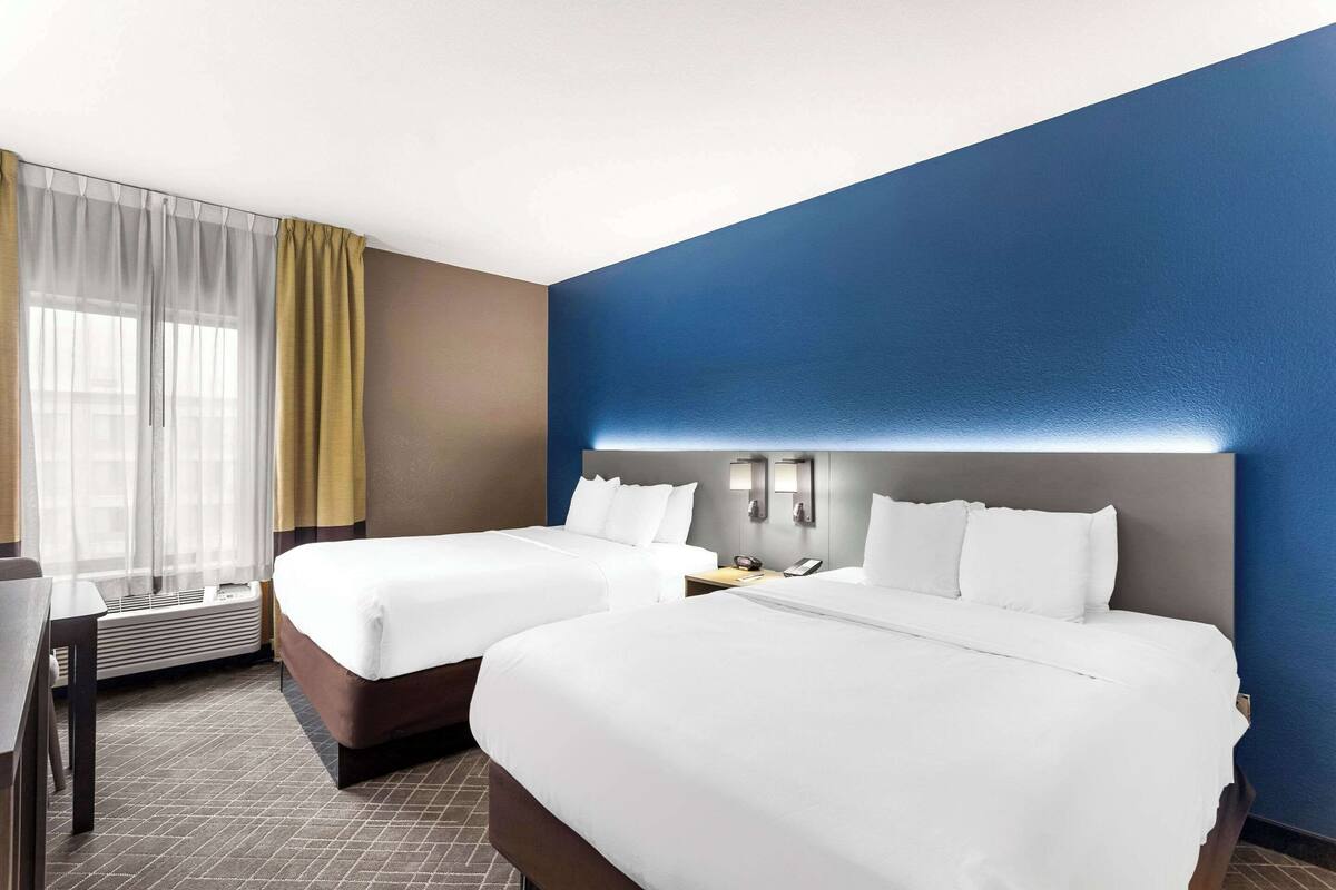 Ein Hotelzimmer mit zwei Betten, einem Schreibtisch und einem Fenster mit Vorhängen.