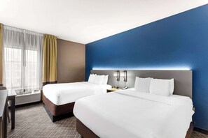 A hotel room with two beds, a desk, and a window with curtains.