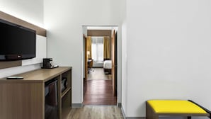 Habitación de hotel con televisión, cafetera y un banco amarillo.