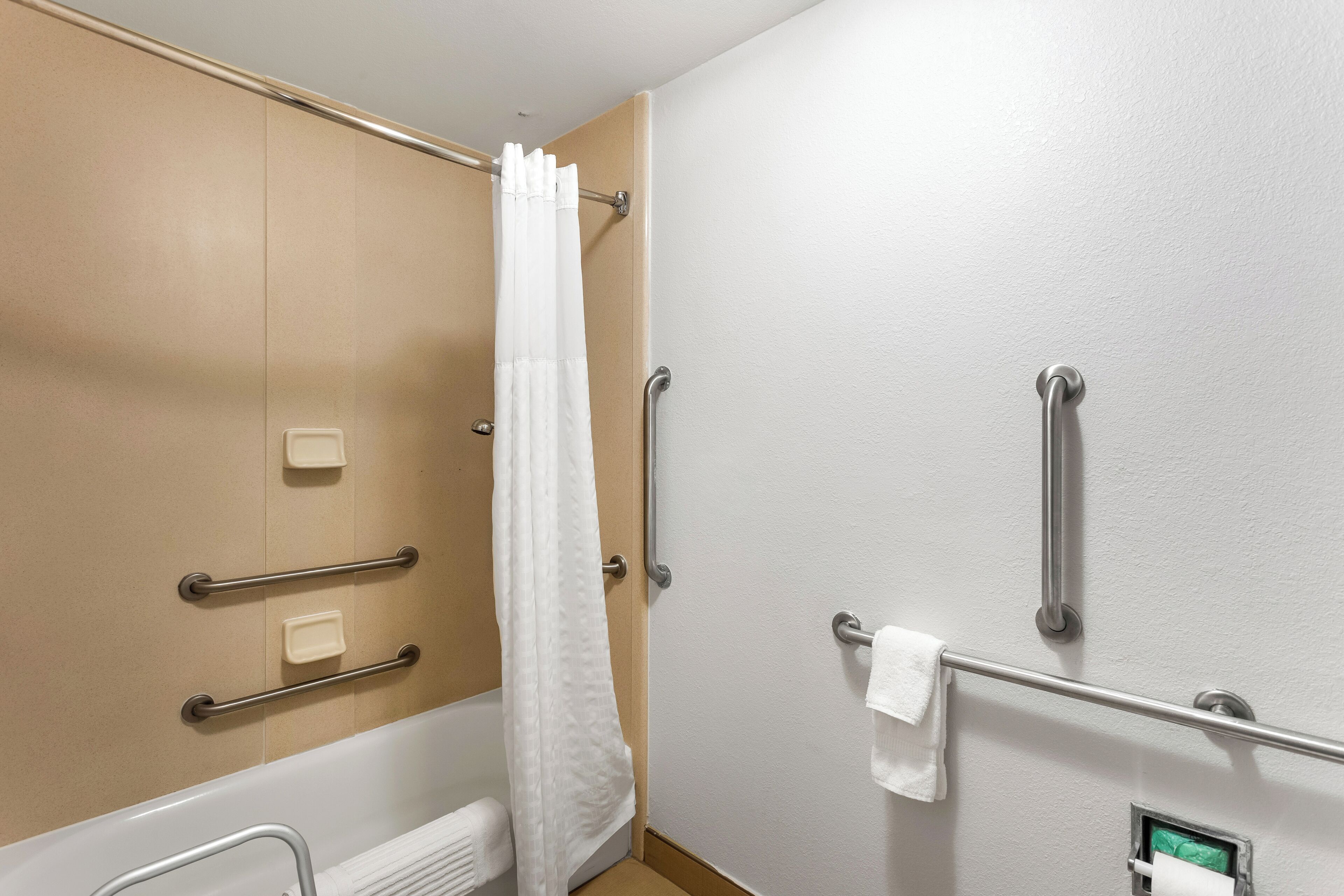 A bathroom with a bathtub, a shower curtain, grab bars, and a towel rack.